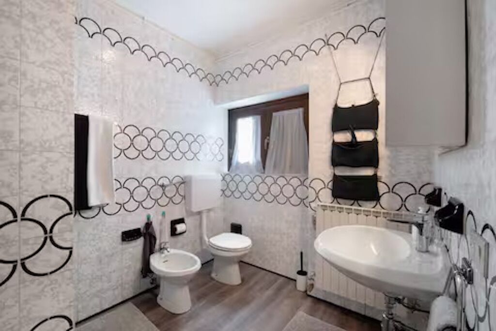 A bathroom with a toilet, bidet, and sink, with decorative wall tiles and a mirror.