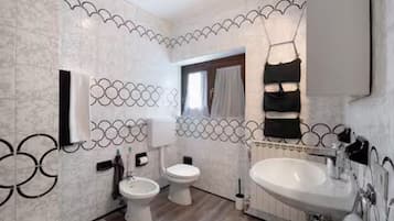 A bathroom with a toilet, bidet, and sink, with decorative wall tiles and a mirror.