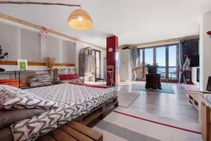 Ein Schlafzimmer mit einem Bett, einer hölzernen Bank, einer Pendelleuchte, einem Kleiderschrank und einem großen Fenster.