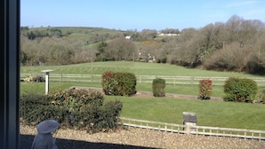 Vista de uma paisagem rural com colinas ondulantes, um campo cercado e algumas casas espalhadas.