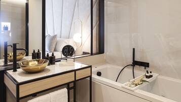 A modern bathroom with a large mirror, a gold bowl sink, a white bathtub, and a towel rack.