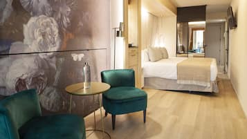 Una habitación de hotel moderna con una cama grande, un sillón verde, una pequeña mesa redonda y un mural floral en la pared.