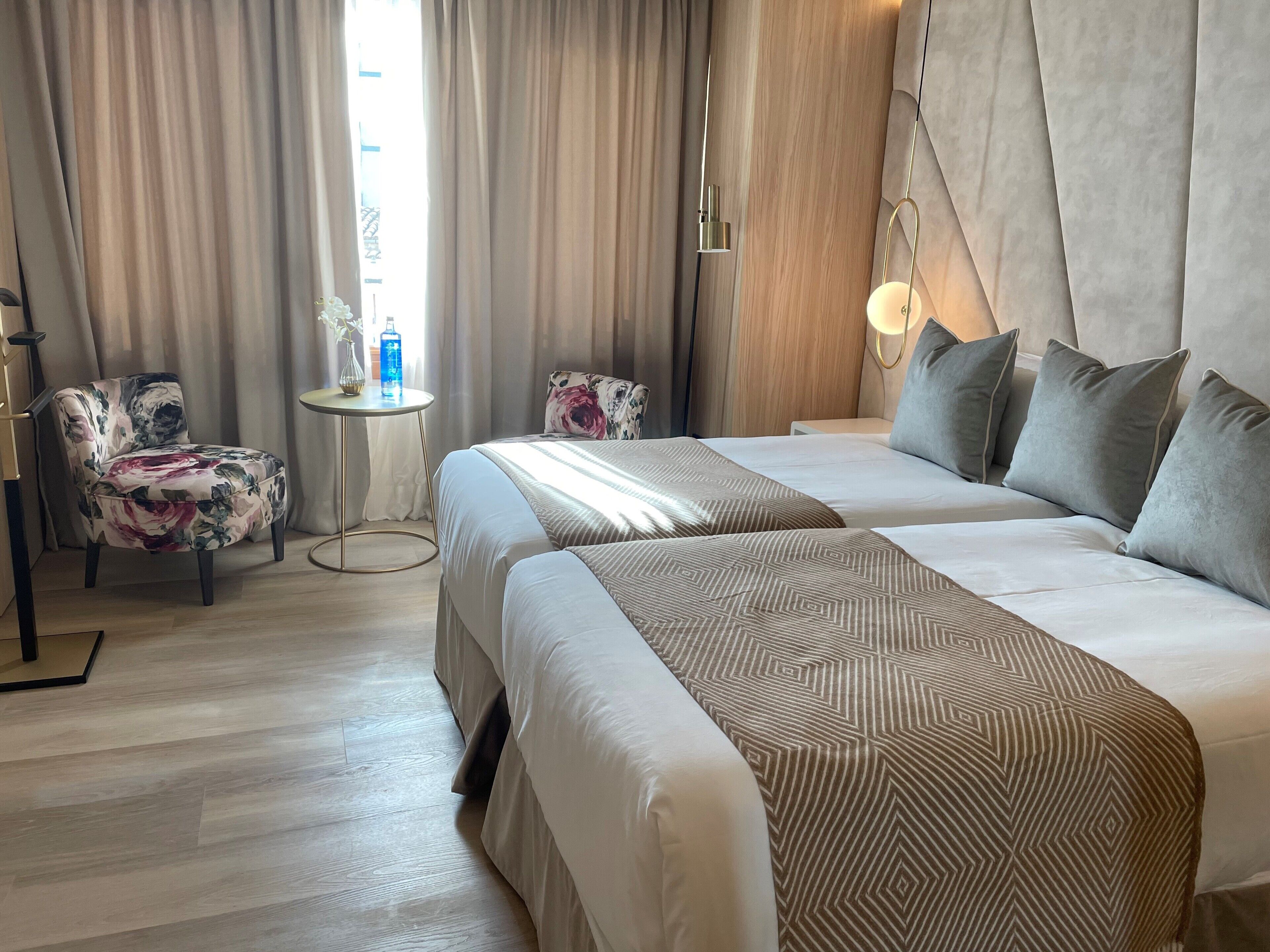 Una habitación de hotel con dos camas, una silla, una mesita y una lámpara.