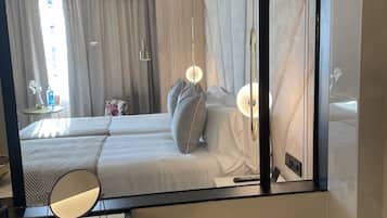 Habitación de hotel con un espejo grande que refleja la cama, una mesita de noche y un baño con bañera y artículos de aseo.