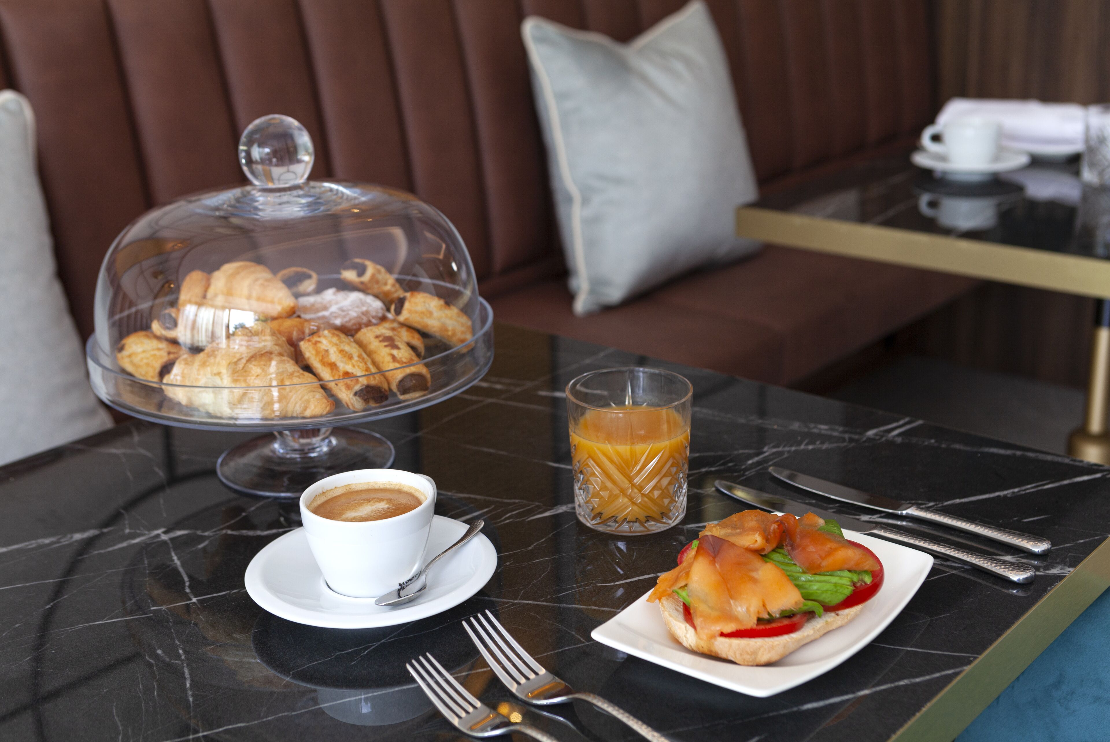 Desayuno con cruasanes, café, jugo y un sándwich sobre una mesa de mármol.