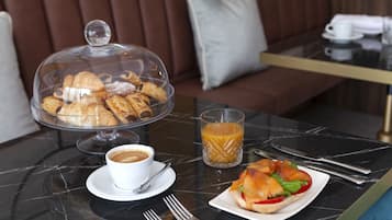 Morgenmad med croissanter, kaffe, juice og en sandwich på et marmorbord.