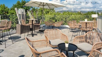 Een terras buiten met rieten meubels, een tafel en een parasol.