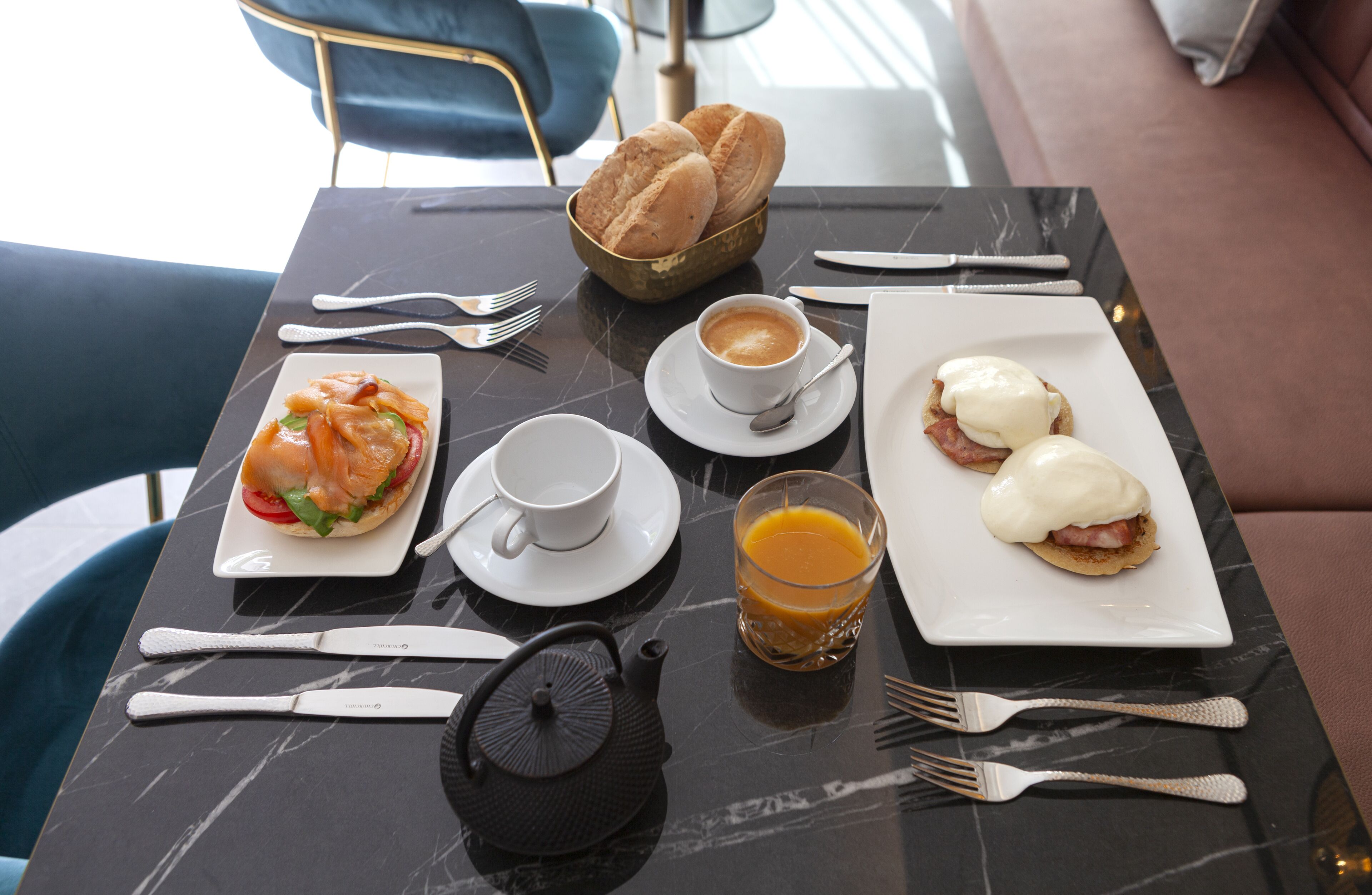 A breakfast setting with a croissant, a sandwich, a cup of coffee, and a glass of orange juice on a marble table.