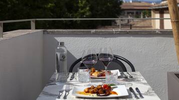 A table set with a plate of food, wine glasses, and cutlery on a balcony with a railing.