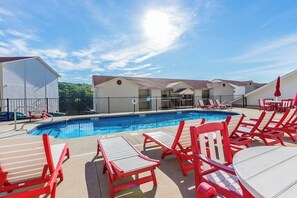 En swimmingpool med röda stolar och bord, omgiven av byggnader med en enkel arkitektonisk stil.