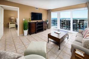 Relax in this spacious living room with a large flat-screen TV, comfortable seating area, and balcony offering a beach view.