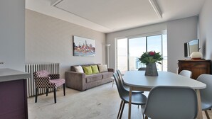 Ein modernes Wohnzimmer mit Essbereich, ausgestattet mit einer Couch, Stühlen, einem Tisch und einem Stadtbild an der Wand.