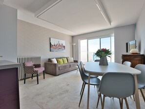 A modern living room with a dining area, featuring a sofa, chairs, a table, and a cityscape painting on the wall.