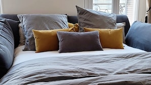 Ein ordentlich bezogenes Bett mit grau-gelber Farbgebung, ein Tablett mit Croissants und Orangensaft, und ein freier Blick auf das Fenster hinter dem Bett.