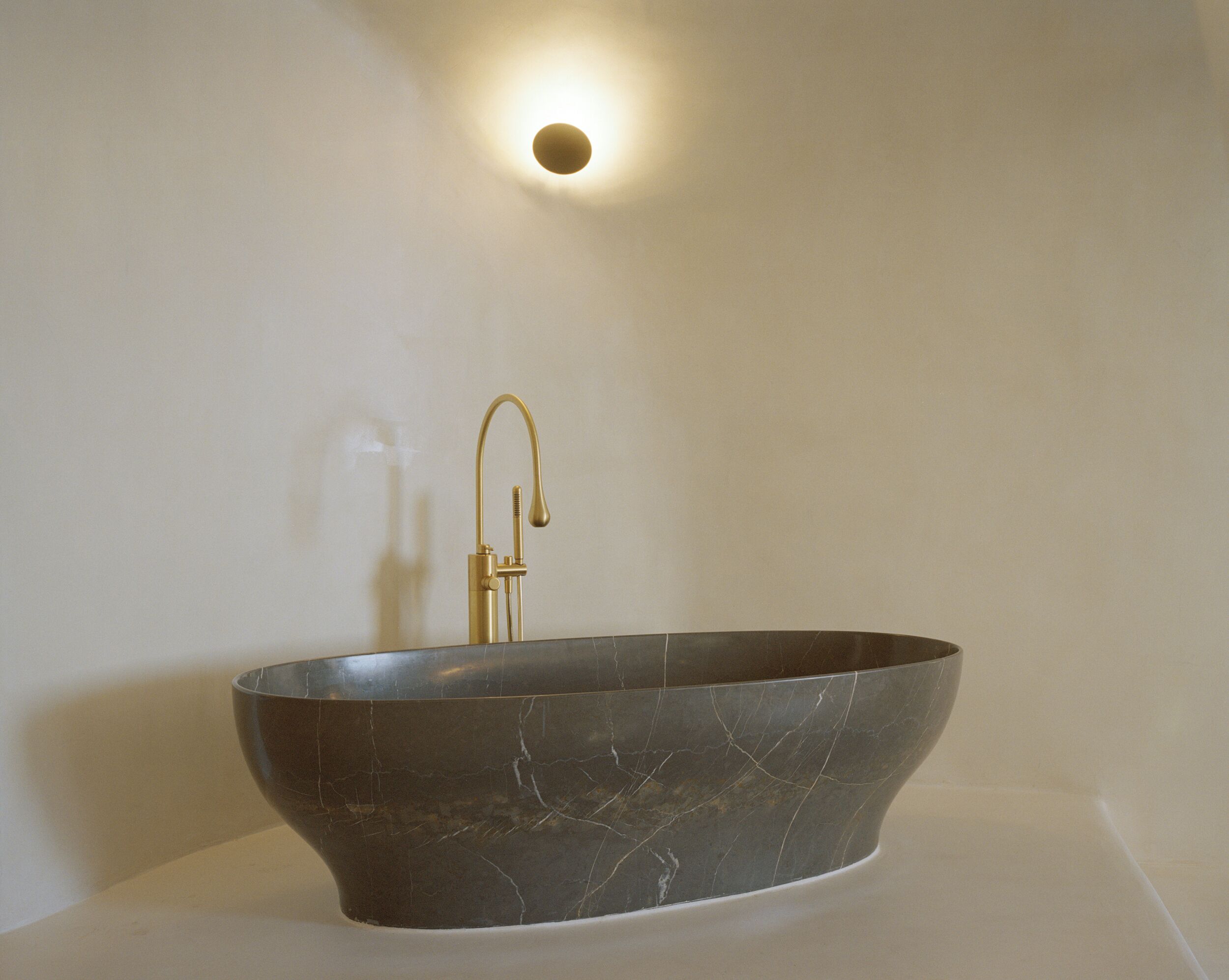 A modern bathroom with a freestanding vessel sink, a gold faucet, and a wall-mounted light.