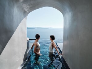 Un couple se détend dans une piscine à débordement privée, avec vue sur la mer et le paysage lointain.