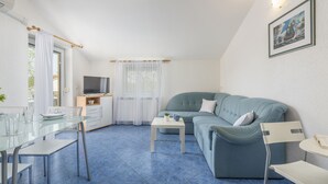 A compact living space with a blue sofa, a glass dining table, a small white table, and a television.