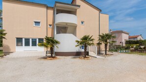 A multi-story building with a central cylindrical structure, surrounded by palm trees and a gravel driveway.