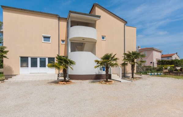 A multi-story building with a central cylindrical structure, surrounded by palm trees and a gravel driveway. - Villa Maja beachfront apartment 4 (Funtana)