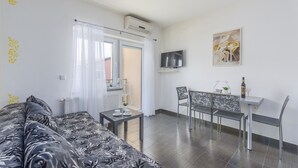 Une pièce moderne comprenant un canapé, une petite table, un coin repas avec des chaises, un téléviseur fixé au mur et un appareil de climatisation.