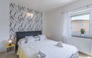 A neatly made bed with white linens and a rolled towel, a bedside lamp, and a wall with a wavy pattern. - Villa Maja beachfront apartment 4 (Funtana)