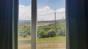 A window view of a landscape with greenery, a road, and distant structures. - Bokor Inn by Sokha Group (Kampot)