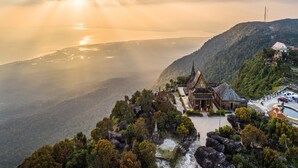 A traditional temple complex with a central building surrounded by trees and rocky terrain, overlooking a valley and a body of water. - Bokor Inn by Sokha Group (Kampot)