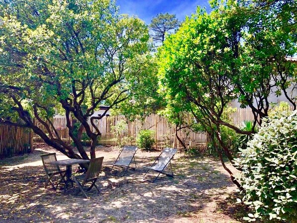 Un patio al aire libre con una mesa y dos sillas, rodeado de árboles y una valla de madera.