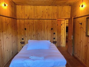 Una habitación con paneles de madera, una cama, dos lámparas de pared y una puerta que da a otra estancia.