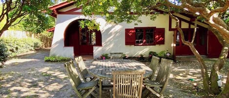 An outdoor seating area with a round table and chairs, surrounded by trees and a building with red accents.