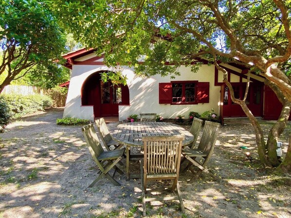 An outdoor seating area with a round table and chairs, surrounded by trees and a building with red accents.