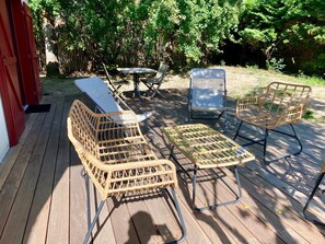 Eine Holzterrasse mit Korbmöbeln, darunter ein Tisch und zwei Stühle.