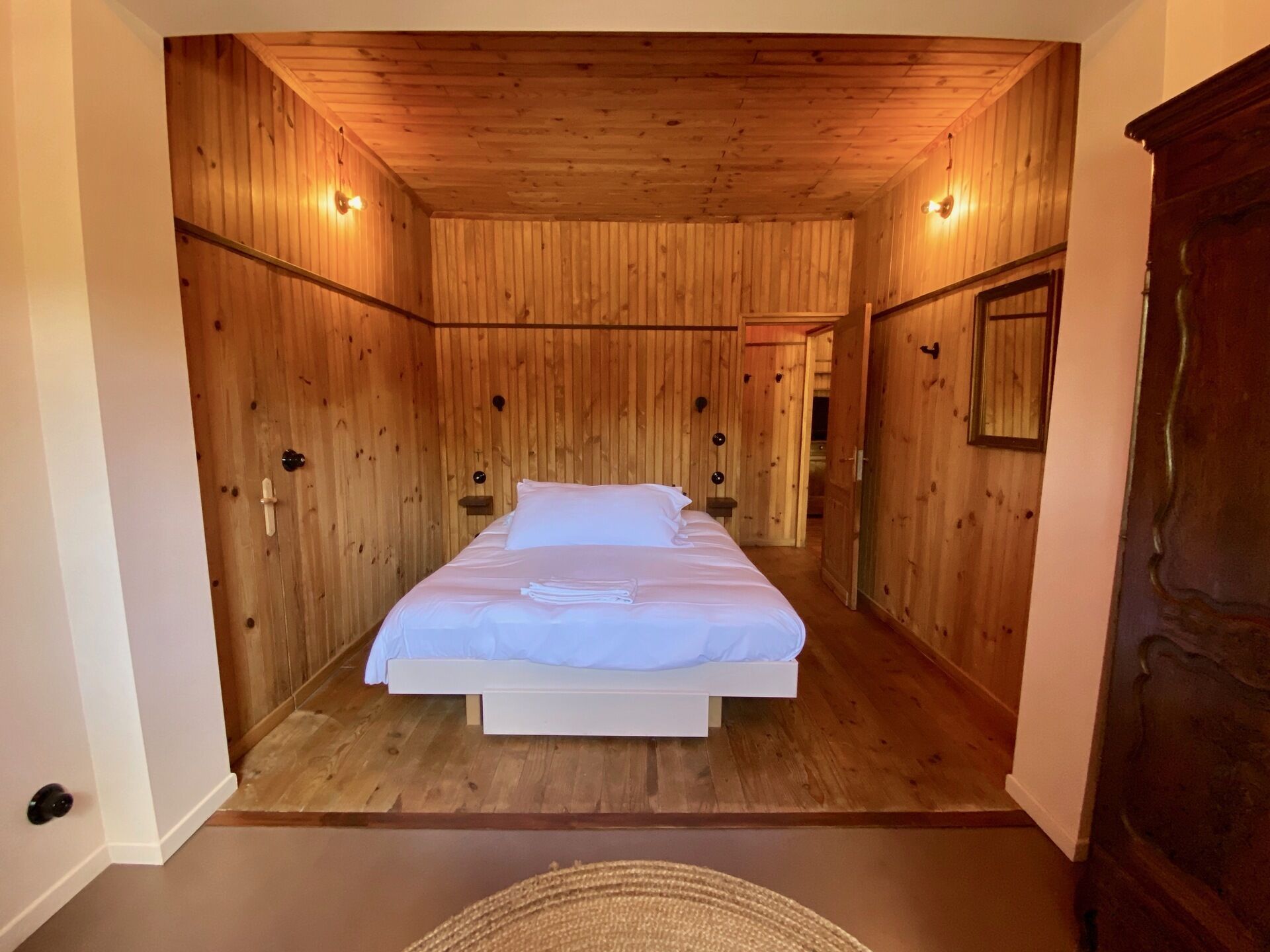 Une pièce aux murs lambrissés, avec un lit, une petite table et un miroir.