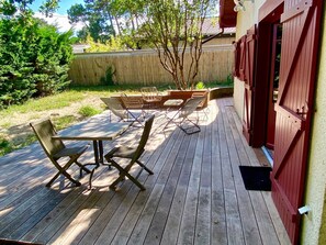 Eine Holzterrasse mit Tisch und Stühlen, ein rotfarbenes, auf einen Stall gestaltetes Gebäude und ein Holzzaun im Hintergrund.