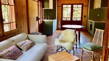 Une pièce confortable avec un canapé, une petite table et une chaise. Une fenêtre offre une vue sur la verdure environnante.