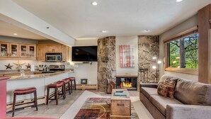 A modern kitchen with a stone accent wall, a fireplace, and a cozy seating area with a sofa and bar stools. - 🏔️Ski Access~Hot Tub~Studio Premier 110🏔️ (Snowmass Village)