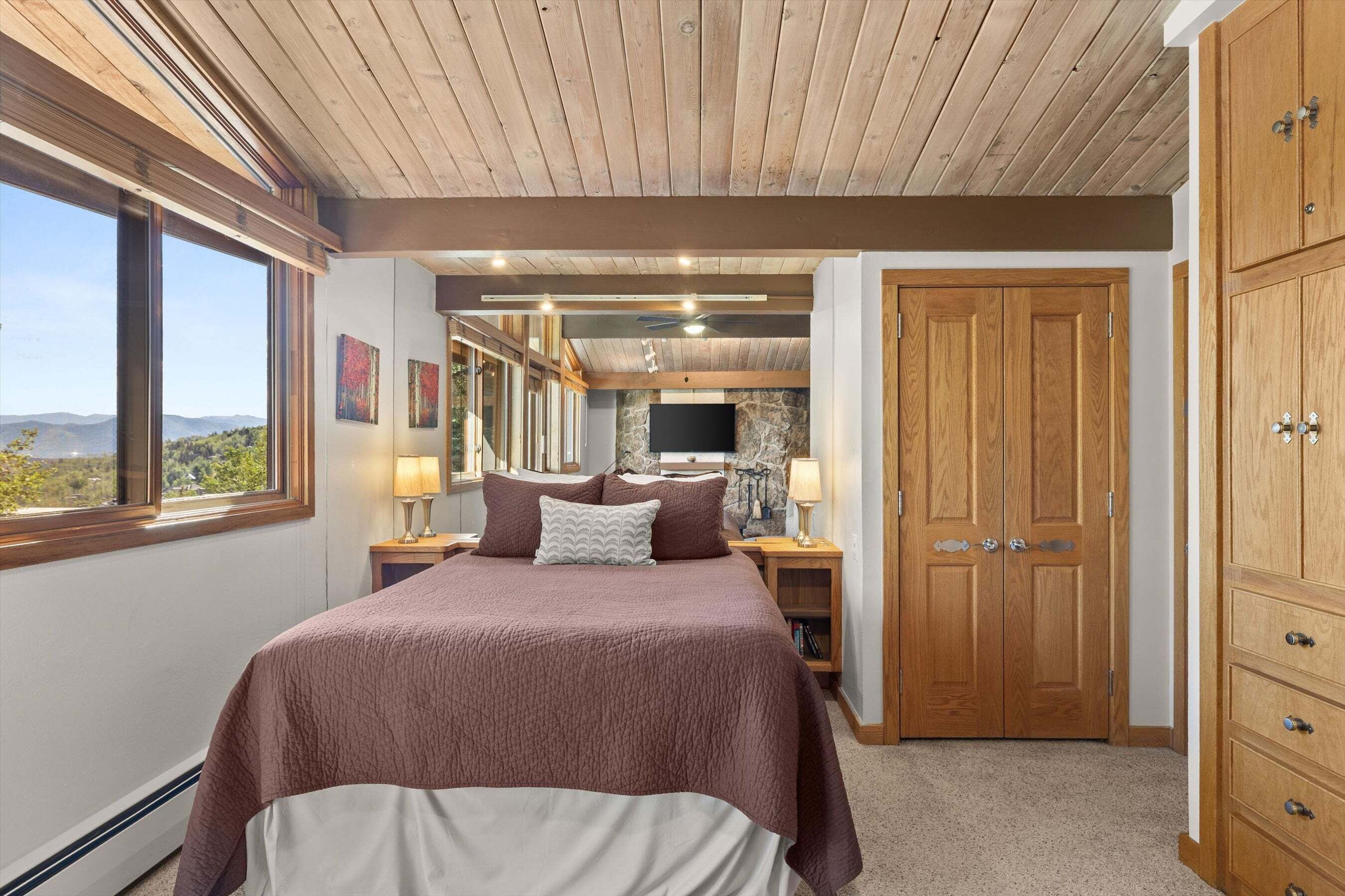 Ein Schlafzimmer mit einem großen Bett, einem Kamin aus Stein, einem Holzschrank und Blick ins Freie.