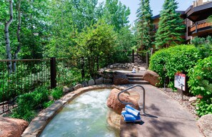 Un área de aguas termales con una piscina de piedra, rodeada de vegetación y una valla de madera.