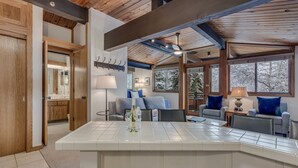 Una cocina moderna con una isla grande, vigas de madera en el techo y ventanas amplias con vistas a árboles.