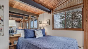 Un dormitorio con una cama grande, vigas de madera en el techo, una ventana con vistas nevadas y un escritorio con una lámpara.
