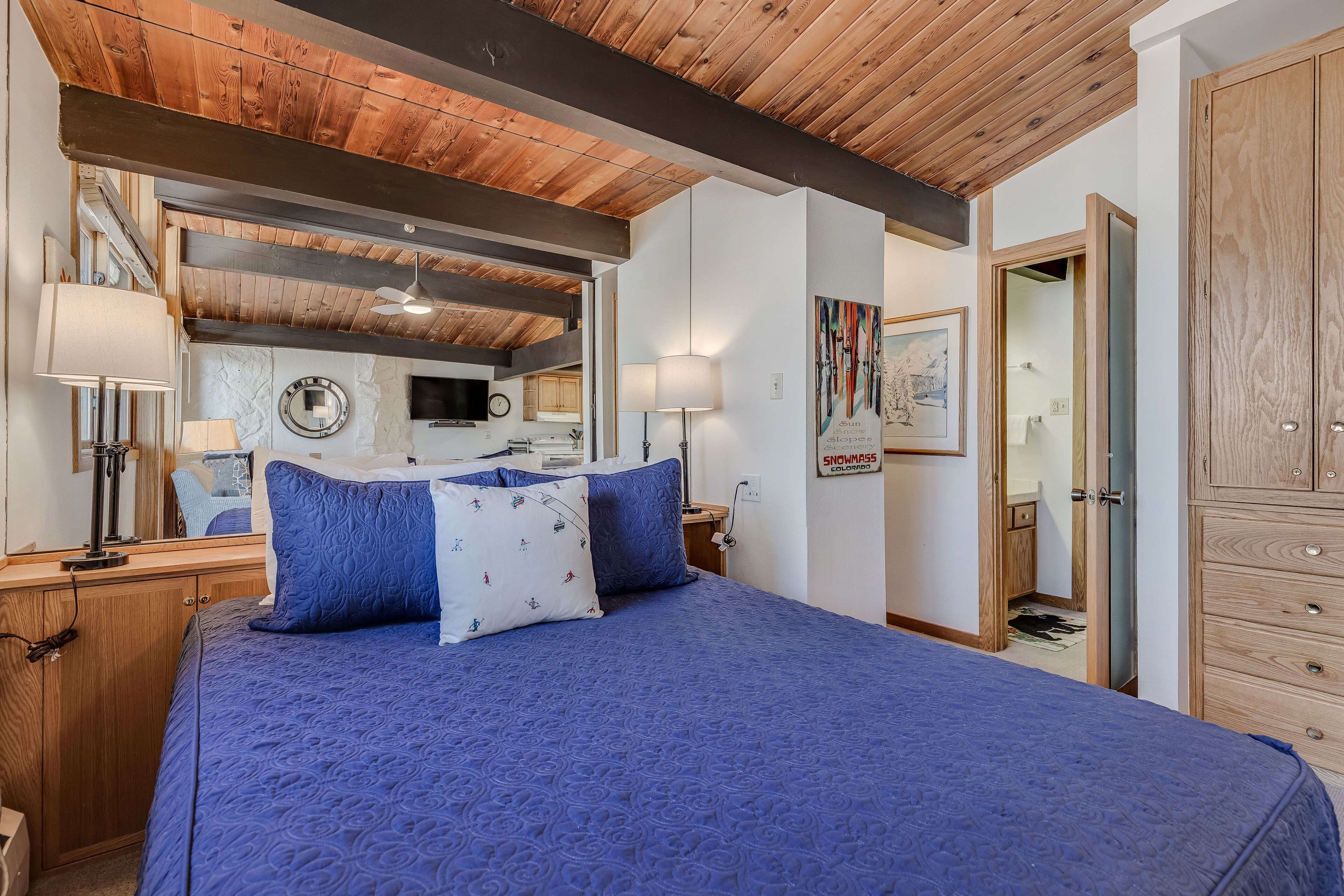 Ein Schlafzimmer mit einem Bett, Nachttischlampen, einer Wanduhr, einem Fernseher und einer Tür zu einem Badezimmer.
