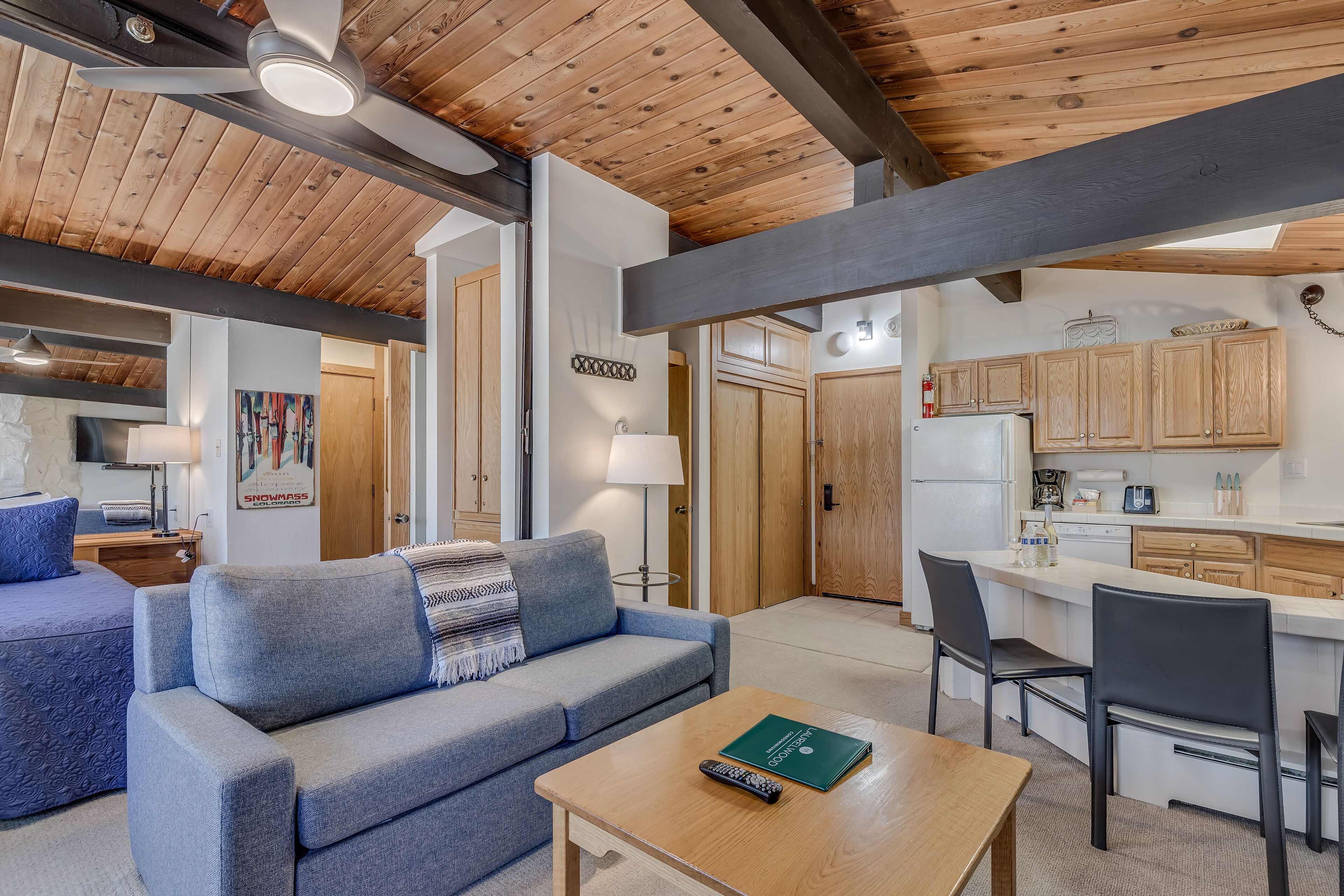 A cozy living area with a sofa, a coffee table, and a kitchen area with wooden cabinets and a refrigerator.