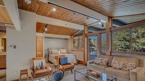 Un salon moderne avec un canapé, des fauteuils et une table basse. On y trouve un lit avec une tête de lit et une fenêtre avec des stores.
