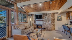 Un salon chaleureux avec une cheminée en pierre, un plafond en bois et de grandes fenêtres.