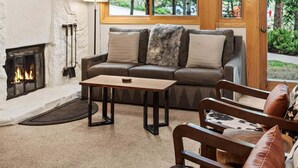 A cozy living room with a fireplace, a sofa, a coffee table, and a view of the outdoors through large windows. - 🏔️Ski Access~Hot Tub~Studio Premier 201🏔️ (Snowmass Village)