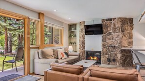 A modern living room with a stone fireplace, a sofa, a coffee table, and a TV mounted on the wall. - 🏔️Ski Access~Hot Tub~Studio Premier 202🏔️ (Snowmass Village)