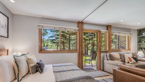 A modern bedroom with a large bed, a sofa, and a window offering a view of trees and a deck. - 🏔️Ski Access~Hot Tub~Studio Premier 202🏔️ (Snowmass Village)