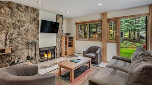 A living room with a stone wall, fireplace, and large windows overlooking a garden. - 🏔️Ski Access~Hot Tub~Studio Deluxe 203🏔️ (Snowmass Village)