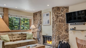 Una sala de estar acogedora con una chimenea de piedra, un ventanal amplio, un televisor de pantalla plana y un sofá cómodo.