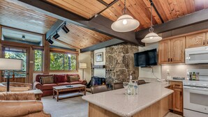 A spacious living area with a large island, wooden ceiling beams, stone wall, and a stone fireplace.